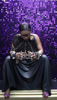 Woman in a black dress sitting on a step with a purple sequin backdrop